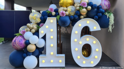 Large illuminated numbers "16" surrounded by blue, gold, and pink balloons with floral decorations.