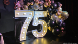 Large illuminated "75" sign surrounded by a decorative arrangement of balloons in various colors.