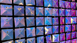 A wall of reflective, iridescent square panels with a diamond pattern arranged in rows and columns.